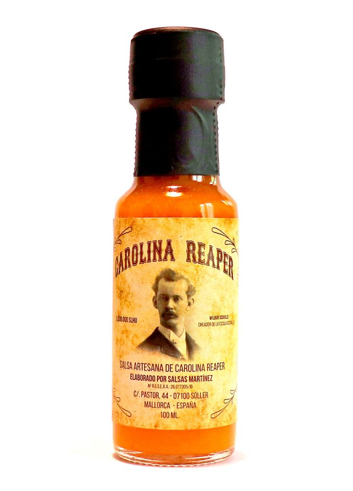 Frasco de 100 ml de salsa picante a base de chile Carolina Reaper, hecho en Soller - Mallorca. Por la variedad de chile la salsa es de tono amarillo anaranjado. Cuello y tapón precintados con lámina plástica de color negro. En la etiqueta un retrato en sepia de un caballero con bigote.