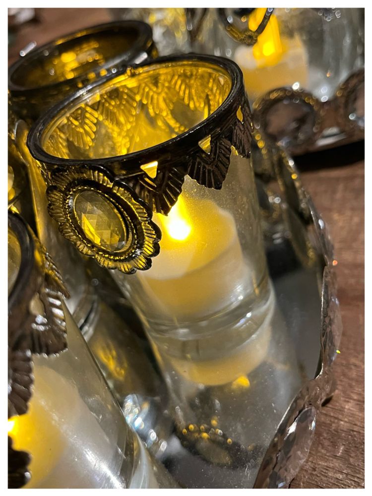 Glazen waxinelichthoudertjes met oud zilveren ornamentjes versierd. Op een spiegeldienblad. Flakkerende vlammetjes.