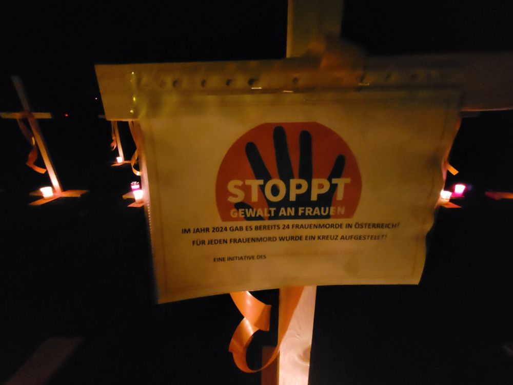 Nahaufnahme eines Kreuzes mit Erklärungszettel, darauf steht: 
STOPPT Gewalt an Frauen
Im Jahr 2024 gab es bereits 24 Frauenmorde in Österreich!
Für jeden Frauenmord wurde ein Kreuz aufgestellt!
Eine Initiative des Soroptimist Club Wiener Neustadt