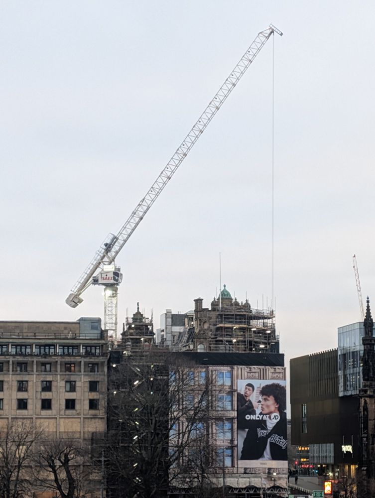 Distance short of a crane lifting a skip onto an office block. The arm is at a notable angle
