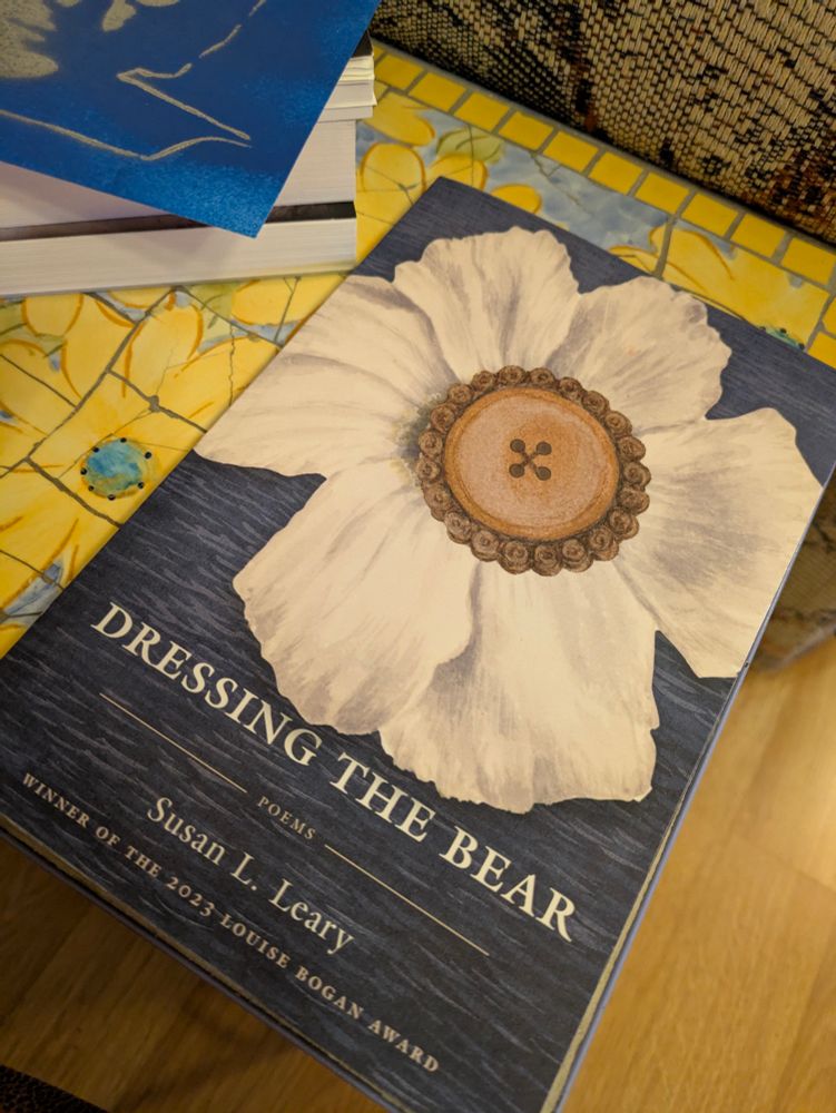 A deep blue book with the illustration of a white flower that has a button for its middle sits atop a tiled table decorated with yellow flowers with light blue middles 