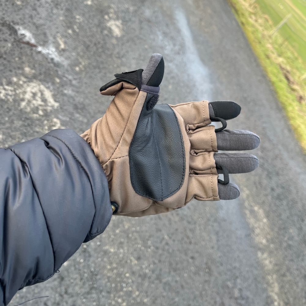 The left hand of a brown and black Heat Company’s Heat 2 Softshell fingerless, foldable mittens with the mitten folded back to reveal a grey Forclaz merino liner glove. 