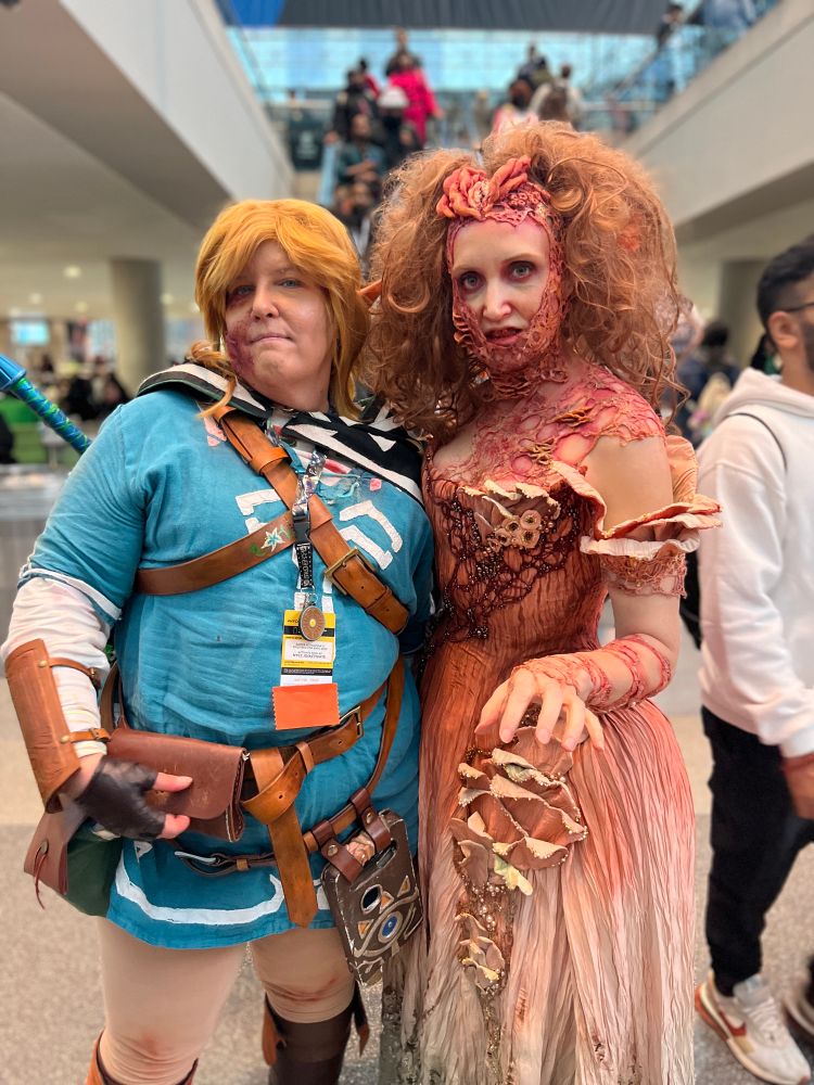 Two cosplayers. The one on the left is dressed as Link from Breath of the Wild. The one on the right is wearing a formal gown with fungal elements, meant to look like a clicker from the game The Last of Us