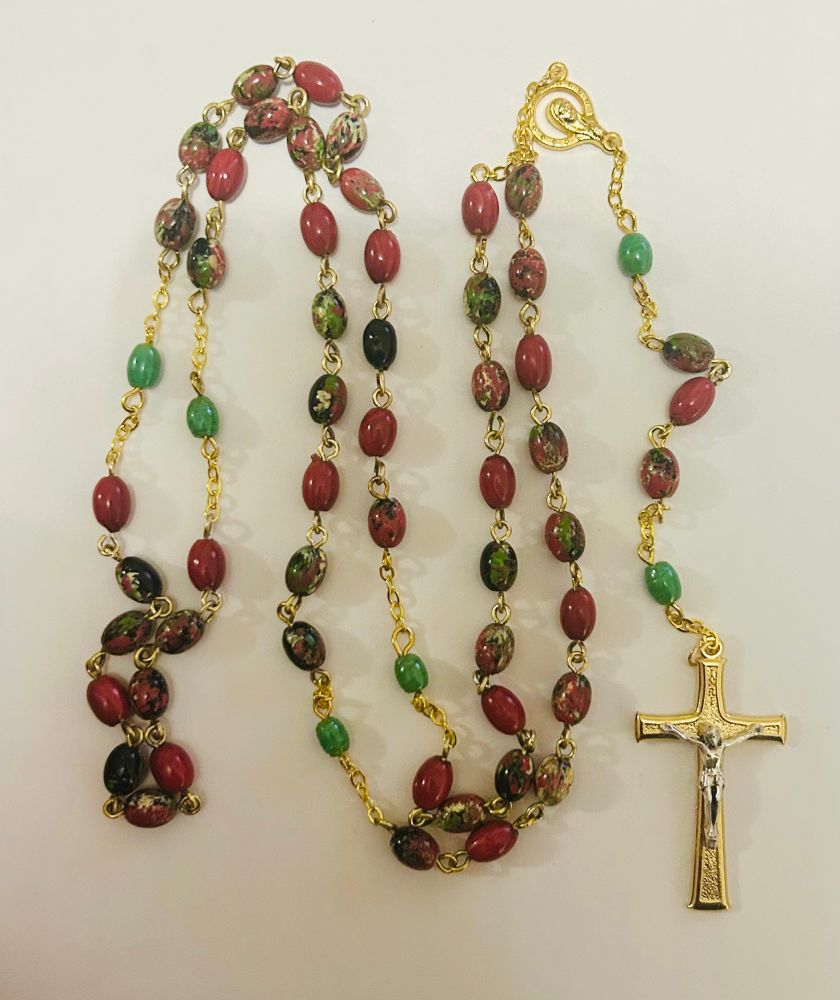 A rosary of oval shaped variegated red beads and gold cross with a silver corpus