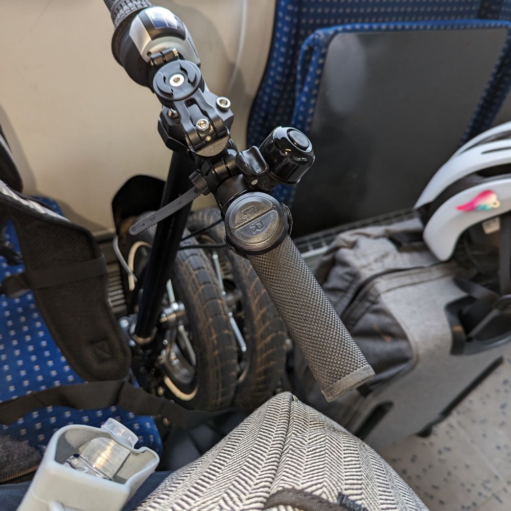 In einer Regionalbahn: vor einem Klappsitz stehen ein kleines Faltrad und ein Koffer, auf dem ein Radhelm zu sehen ist.