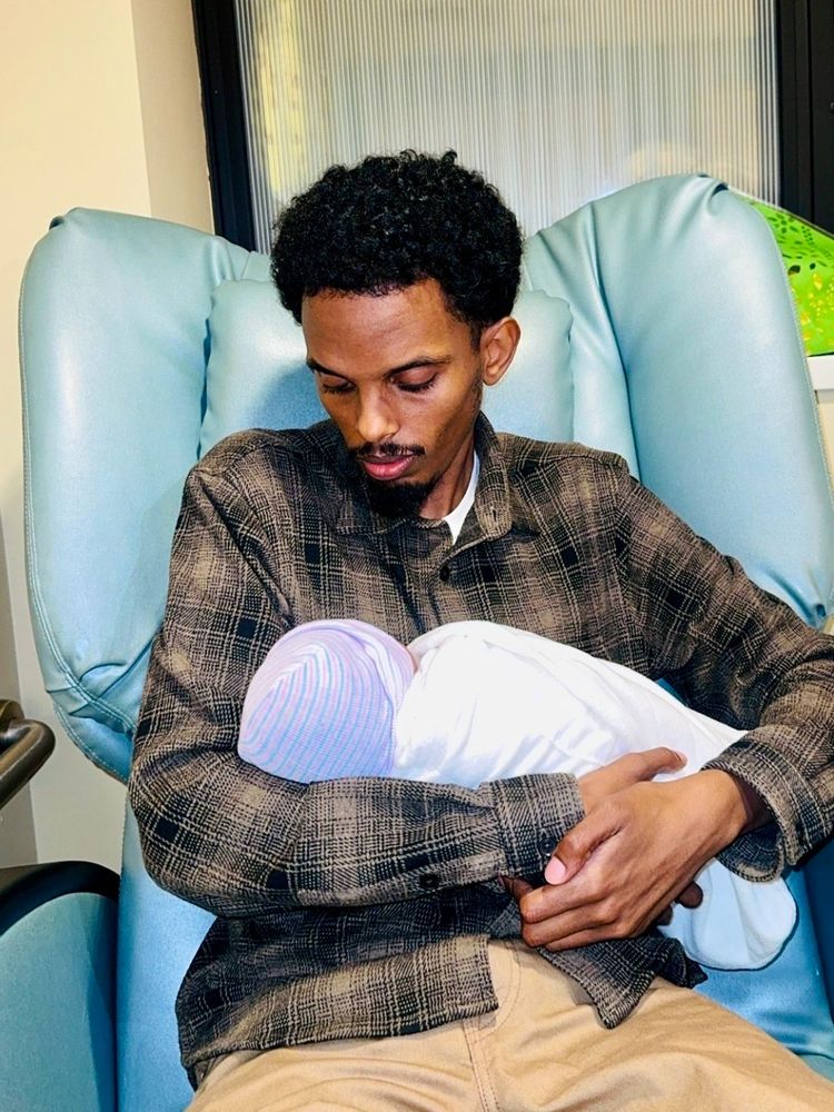 Omar Fateh sitting in a chair and holding his newborn son. 