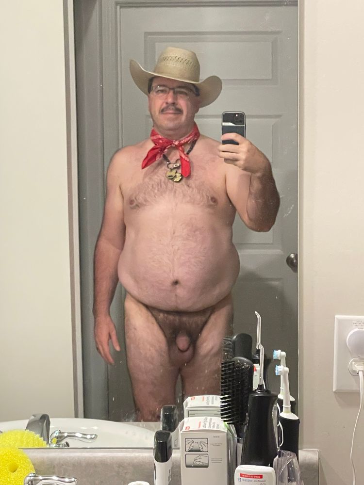 Nude man wearing straw cowboy hat and red hanky tied around neck.