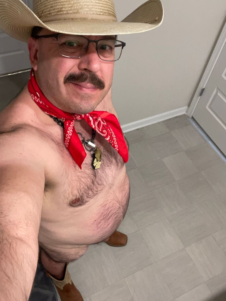 Naked man standing while wearing cowboy boots and cowboy hat.