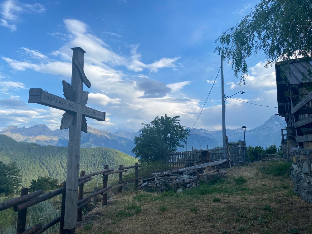 Photo d’un paysage de montagne avec une croix en bois et une barrière en bois, ciel bleu nuageux