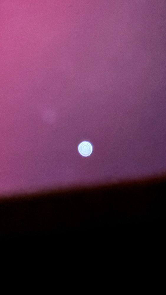 Shining and shimmering bright white dot on greyish purple background. 