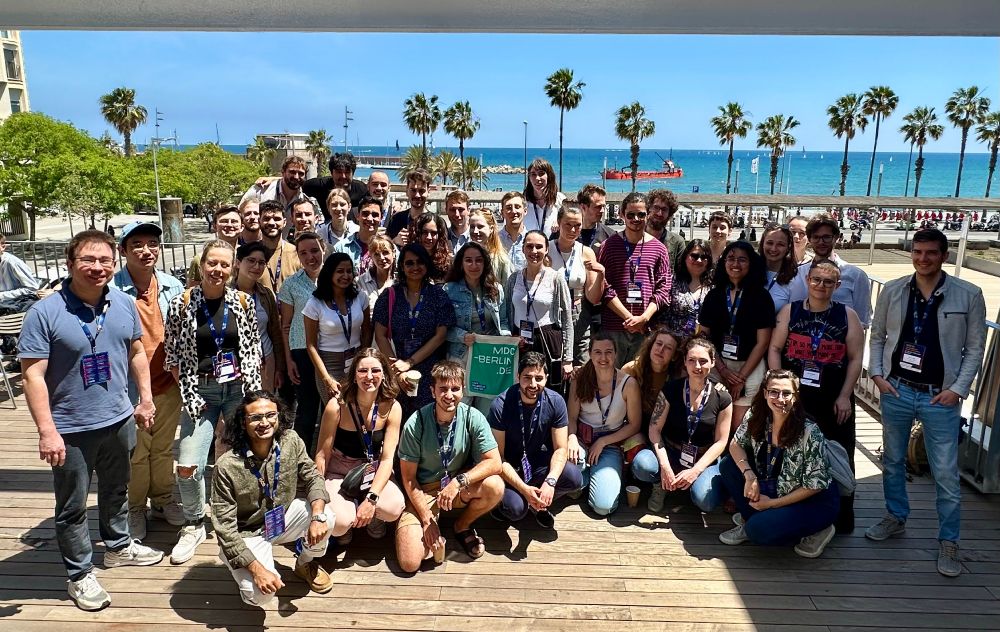 Das Gruppenfoto zeigt 45 Personen auf einer Holzterrasse vor einer Straße, Palmen und dem Meer.
Bildrechte bei Ashley Sanders, MDC