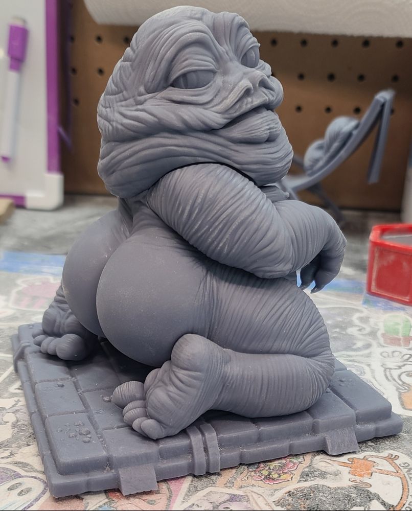 A grey unpainted 3D printed fan art figurine of Star Wars' Jabba the Hutt in a suggestive flirty pose with fully defined feet and a loin cloth on a flat base. The figure is safe for work and can be resized as a fun novelty gift. 