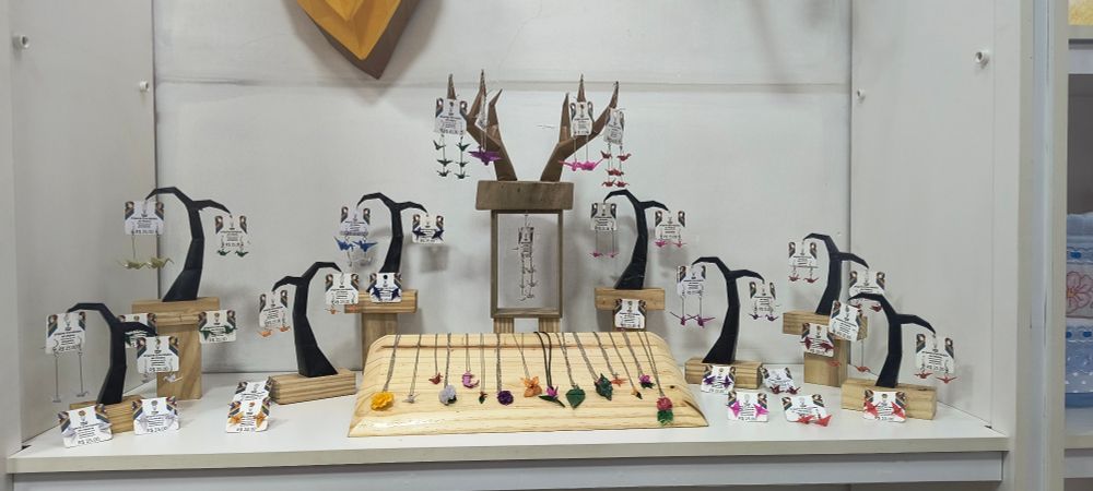 Nicho de loja com expositores de acessórios feitos de origami. Os expositores têm formatos que lembram uma cauda de baleia, e um central que possui um formato de chifres de veado.