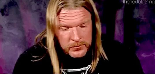 a man with long blonde hair and a beard is wearing a black shirt and making a funny face .