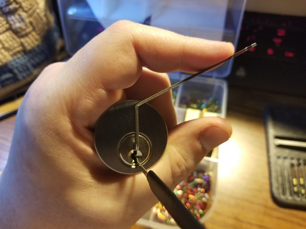 A hand holding a lock cylinder, with a tension tool and lockpick.