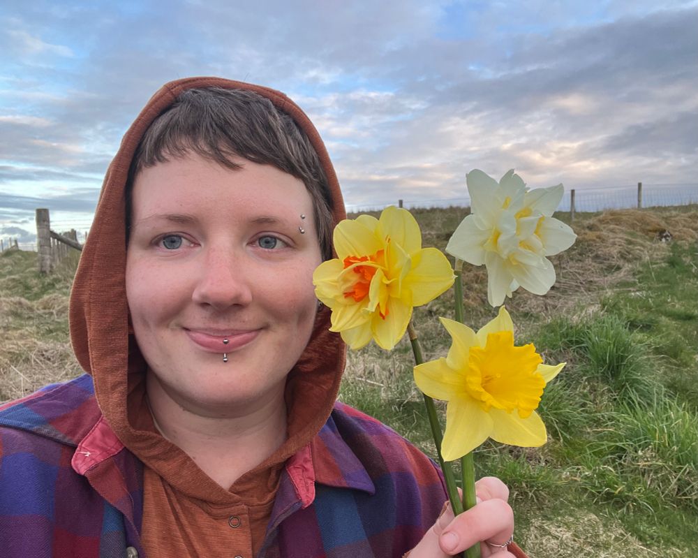 A selfie of a person smiling and holding three distinctive daffodils.