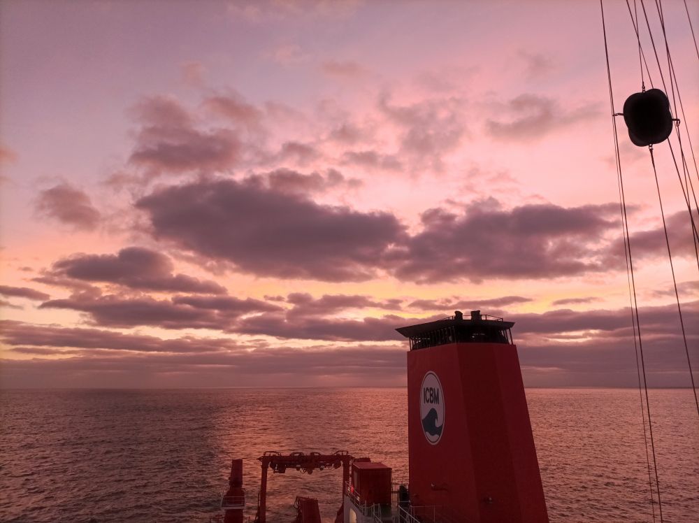 Pink-orange sky with some pretty clouds, the ocean and some parts of the ship in the frame.