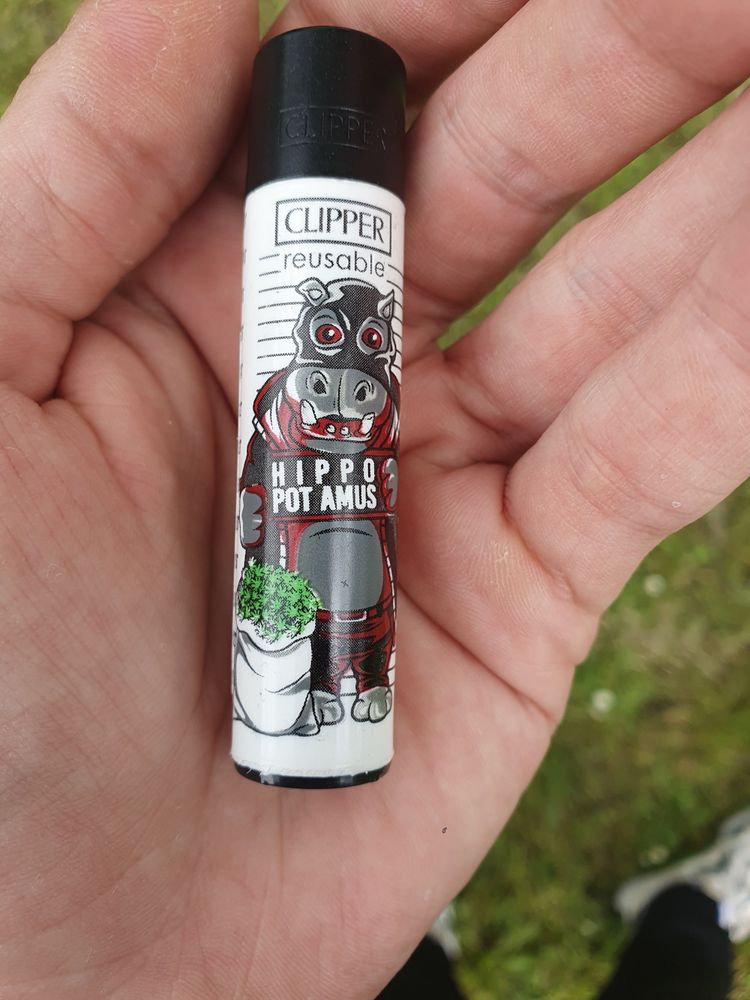 Clipper Feuerzeug, Motiv ist ein Nilpferd mit Sack voller Cannabis in einer Pfote, in der anderen hält es ein Schild auf dem "Hippo Pot Amus" steht.