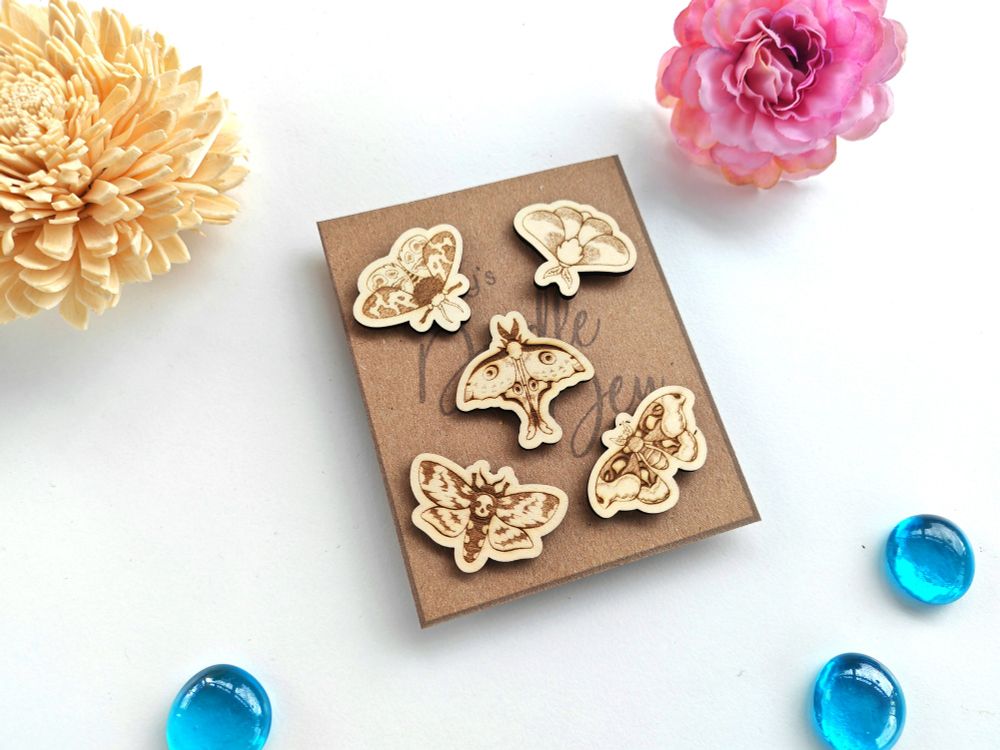 5 wooden engraved moth pins of various species arranged on a piece of kraft paper 
