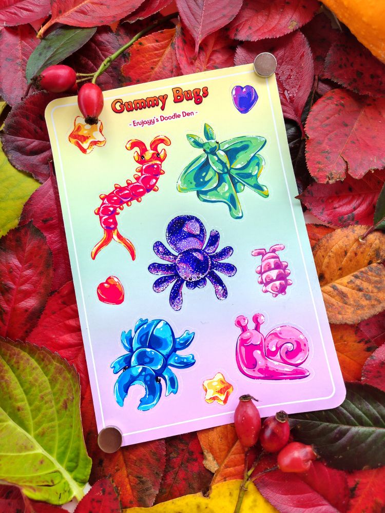 A sticker sheet on top of colourful fallen leaves.
It says: "Gummy Bugs. Erujayy's Doodle Den."
It presents various bugs drawn as gummy sweets. There's a moth, snail, beetle, cebtipede, stars and hearts, and a sour gummy spider.
