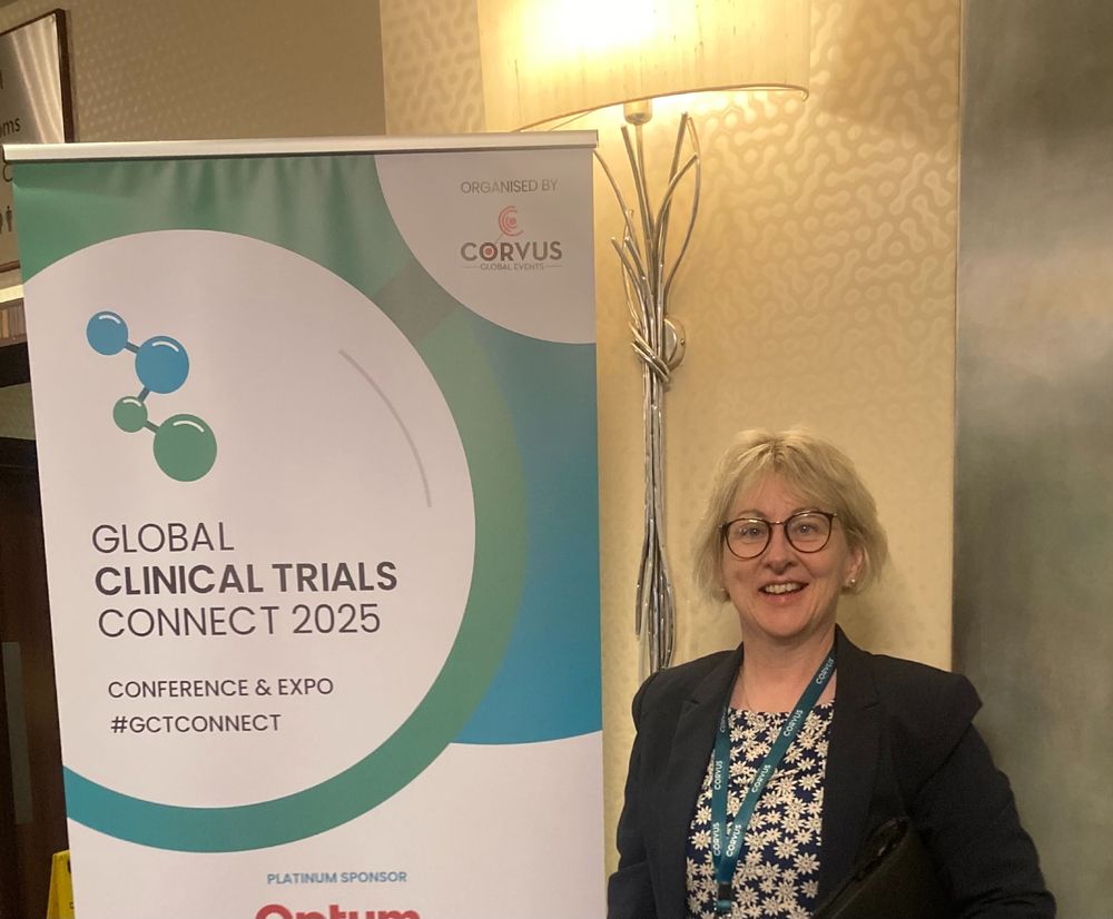 The CRF-UCC Interim Director standing next to a banner for the Global Clinical Trials Connect 2025 Conference.