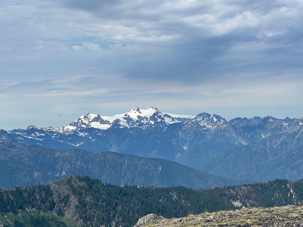 A view of snow covered mountains in the distance beyond several forested river valleys.