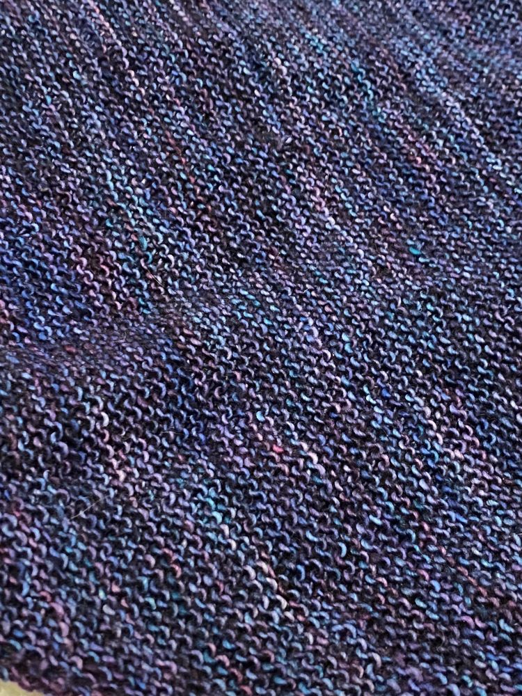 A close-up shot of knit stitches in purple-blue yarn.