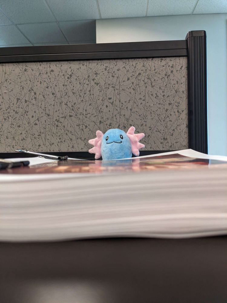 Eye level, side view of a stack of pages, with a beta wooper plush sitting behind it.