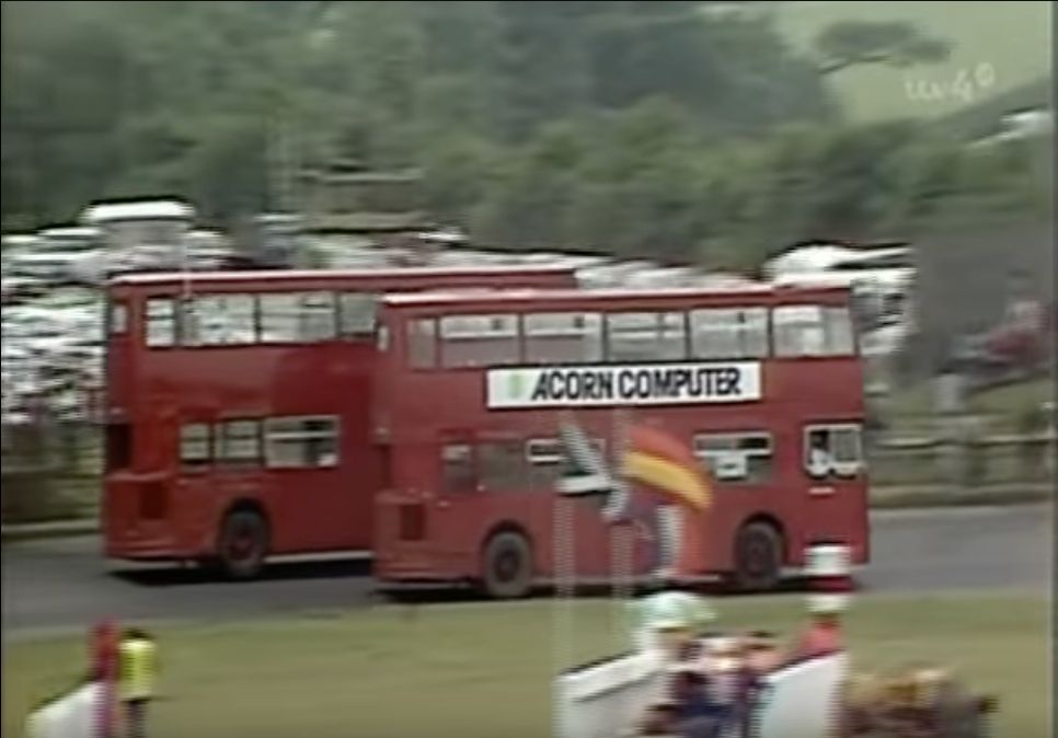 A screen capture of two London double-decker busses on a race circuit in 1982.  One bus has an Acorn Computer advertising board on the side.
