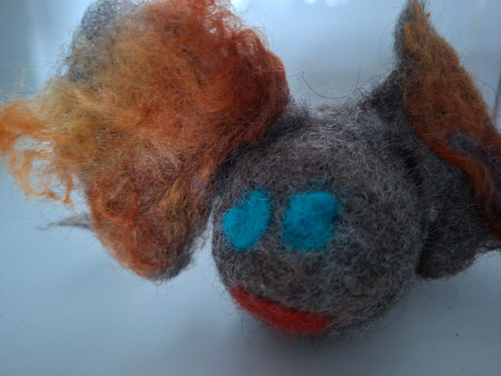 Isokorvainen, harmaa villaolio. Siniset silmät, korvissa oranssikeltaista lankaa.