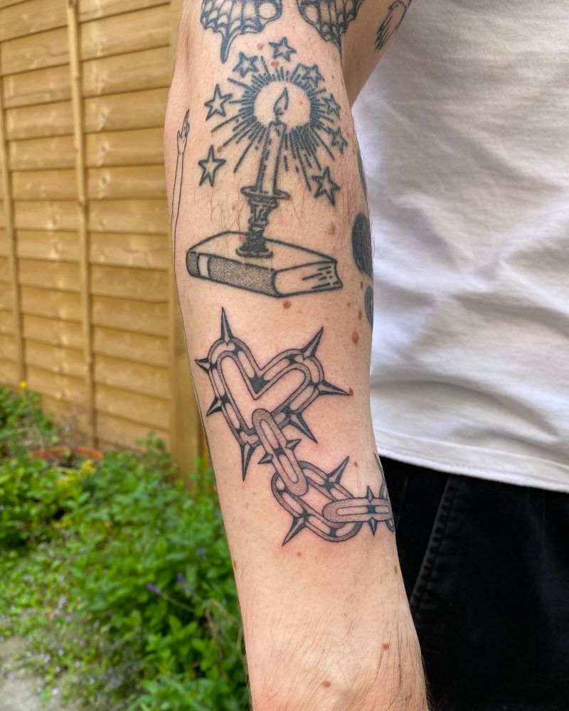 a new tattoo of a spiked chain ending in a heart-shaped link. above it, a healed tattoo of a candle with a starry halo resting on a book