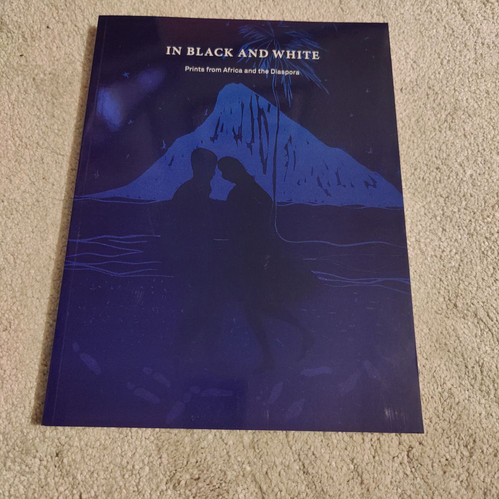 Front cover of book. In Black and White: Prints from Africa and the Diaspora. Cover is a blue print of two shillouetted figures dancing on a beach. 