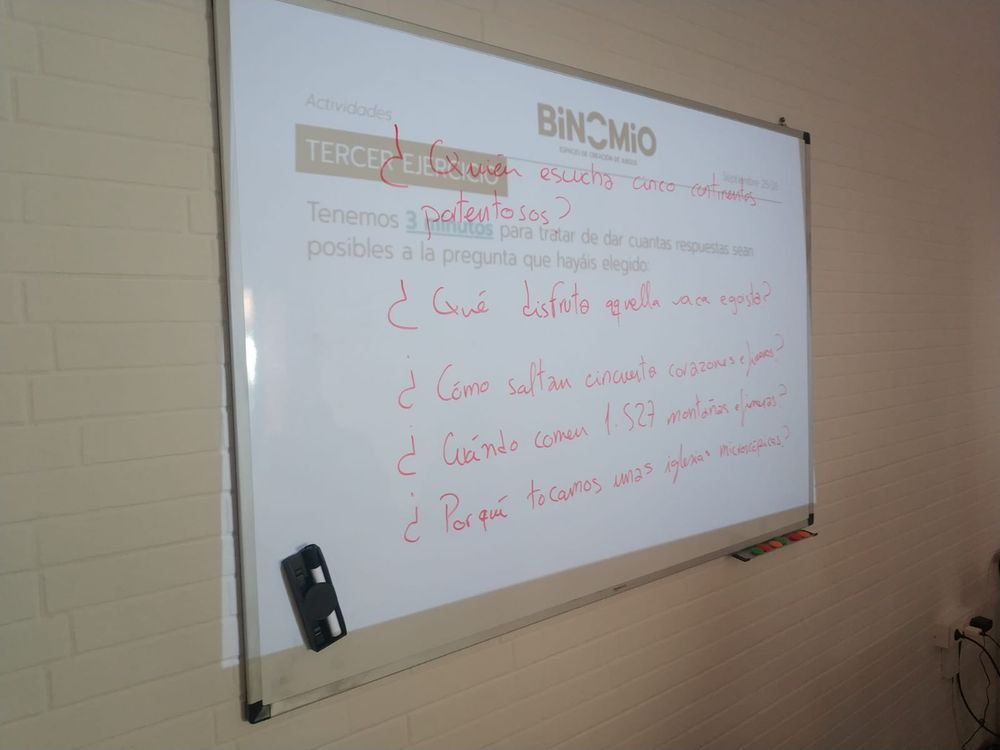 Pizarra de Binomio con varias frases escritas como resultado de un proceso creativo basado en un cadáver exquisito, con el objetivo de generar ideas para los juegos-poema. Se propusieron las siguientes preguntas: 
- ¿Quién escucha cinco continentes portentosos?
- ¿Qué disfruta aquella vaca egoista?
- ¿Cómo saltan cincuenta corazones efímeros?
- ¿Cuándo comen 1527 montañas efímeras?
- ¿Por qué tocamos unas iglesias microscópicas?