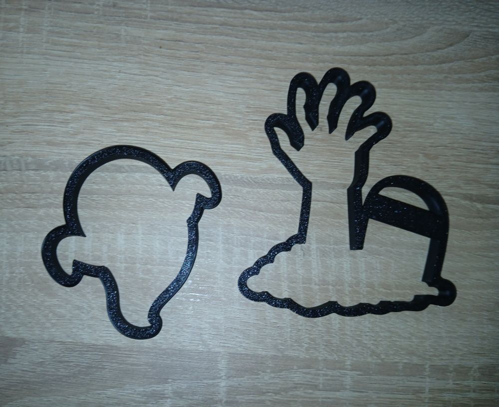Ein Keksausstecher in Form eines Geistes, ein Keksausstecher in Form einer ausgestreckten Hand neben einem Grabstein. 
