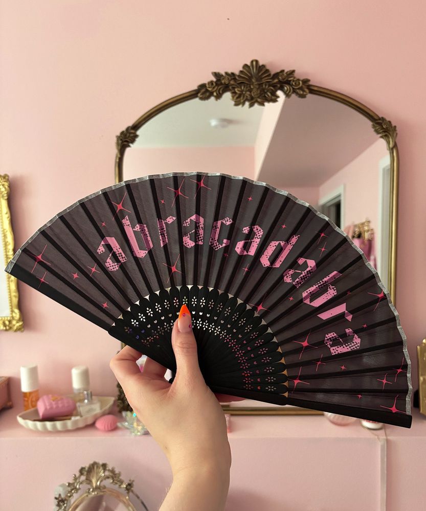 photo of a black fan that reads 'abracadabra' in pink with red sparkles