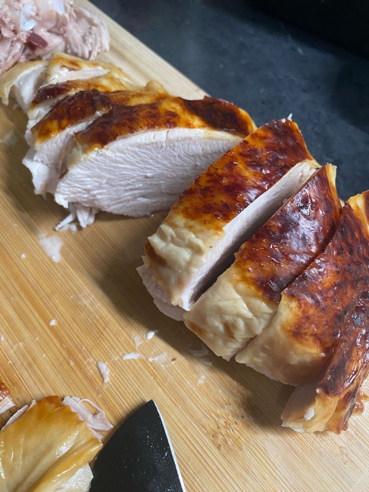 Cooked turkey breast with skin on cut into pieces and layered on a cutting board