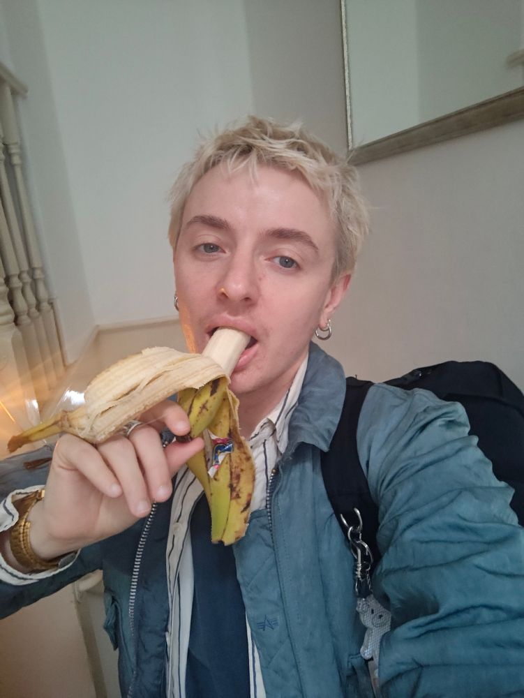 blonde boy eating banana with a coat and bag on
