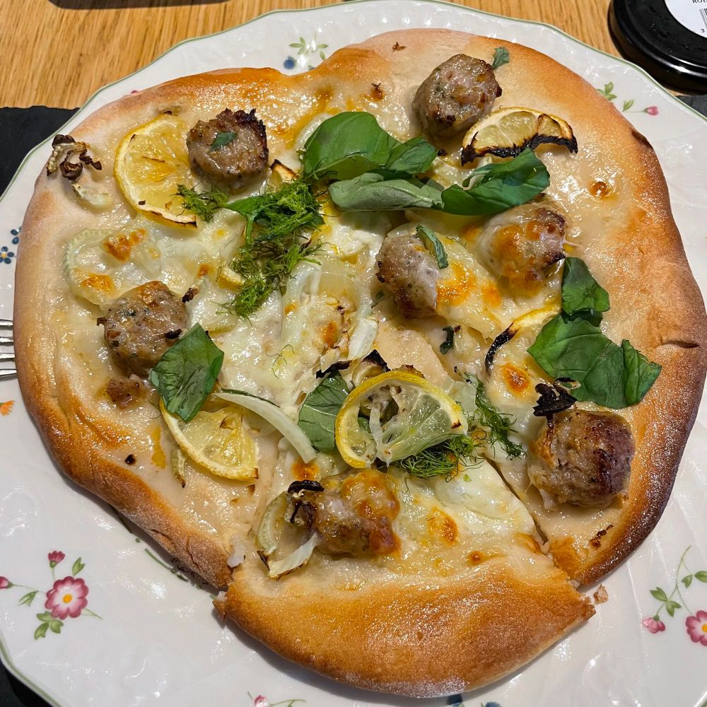 Slightly misshaped homemade pizza with sausage pieces, lemon, fennel and mozzarella (no tomato). 