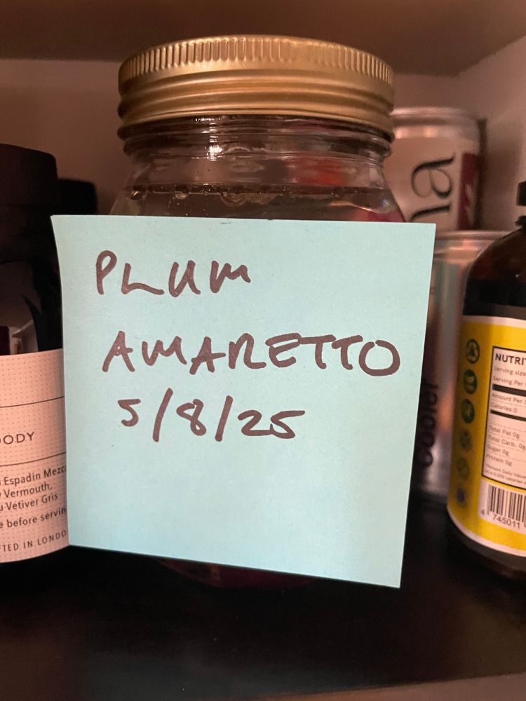 A Kilner jar with a post it note stuck to it, with Plum Amaretto and today’s date written on it. 