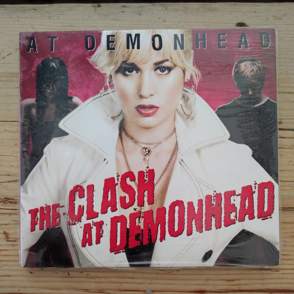 Fully correct CD cover for "At Demonhead" by The Clash At Demonhead, featuring a trio consisting of Brie Larson, Tennessee Thomas and Brandon Routh.