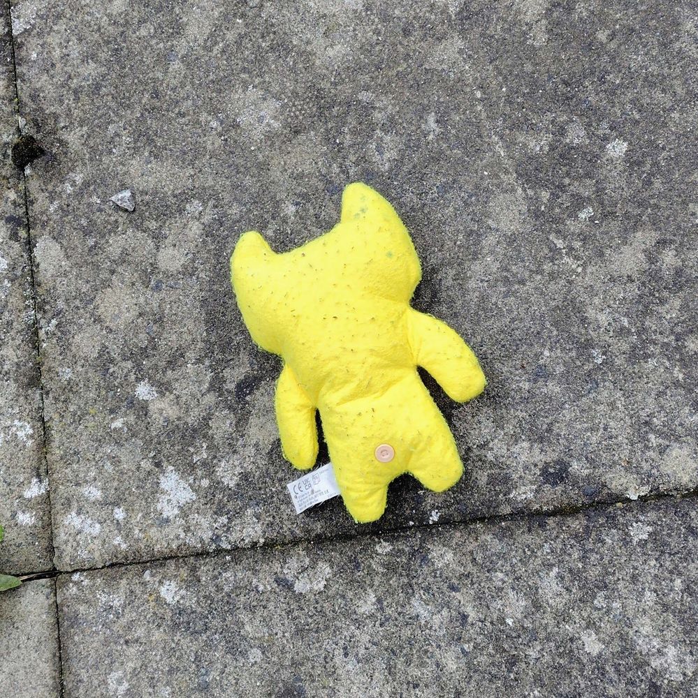 A bright yellow plush face down on the pavement. It has a little pink button for a butthole