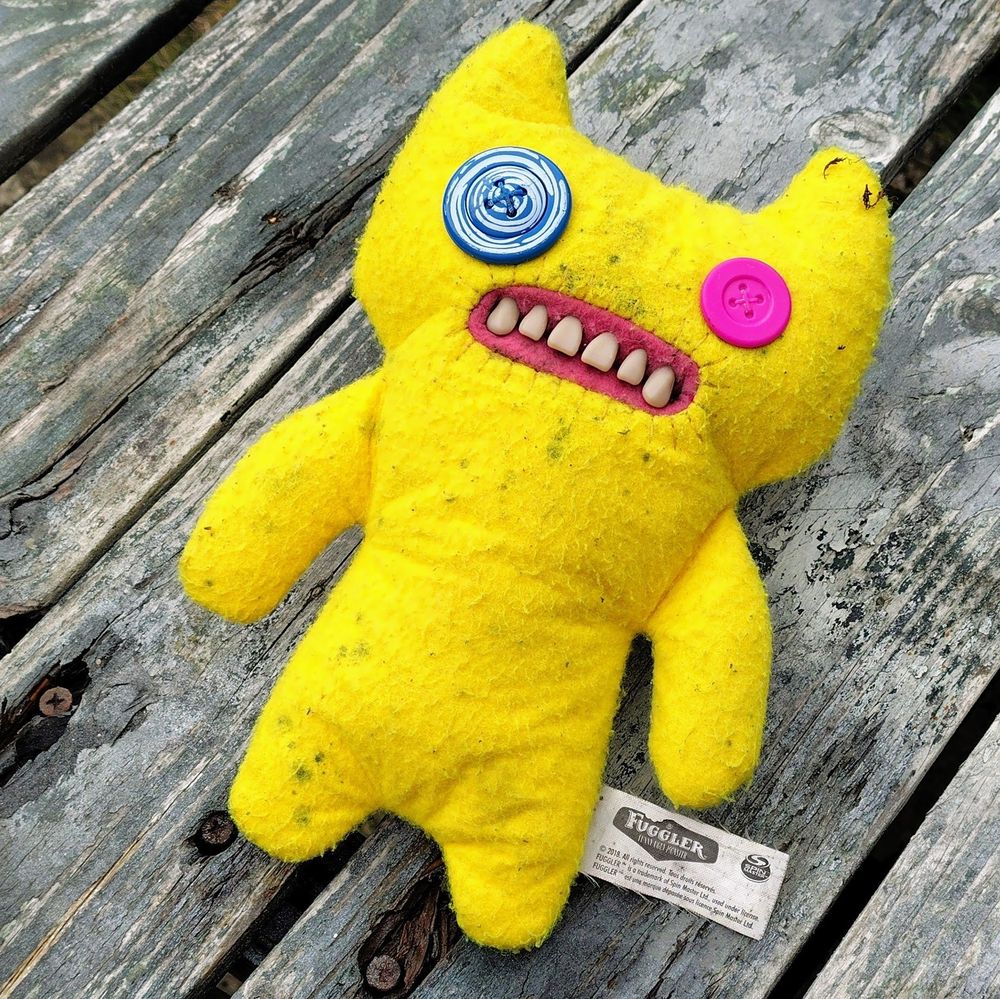 A grody yellow plush 'fuggler' toy it has mismatched button eyes and disturbingly realistic teeth.