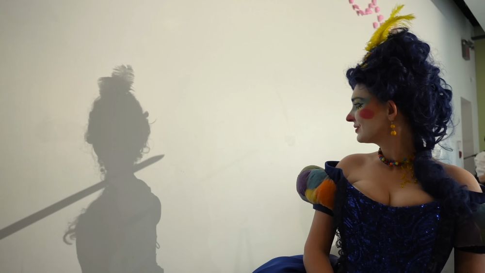 Marie Antoinette looking at her shadow, where her neck is being crossed by a sword