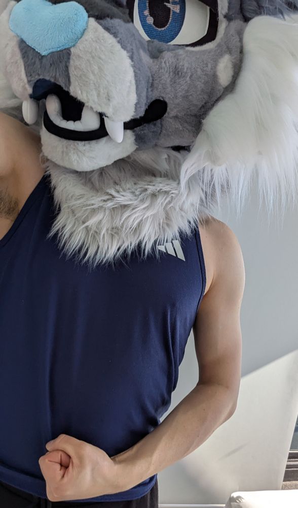 A man wearing a fursuit head flexing his arm muscles