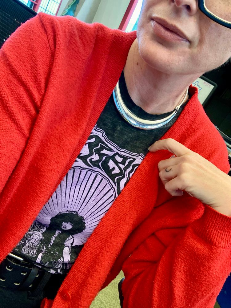 D wearing a red cardigan over a purple and gray Kate Bush shirt.