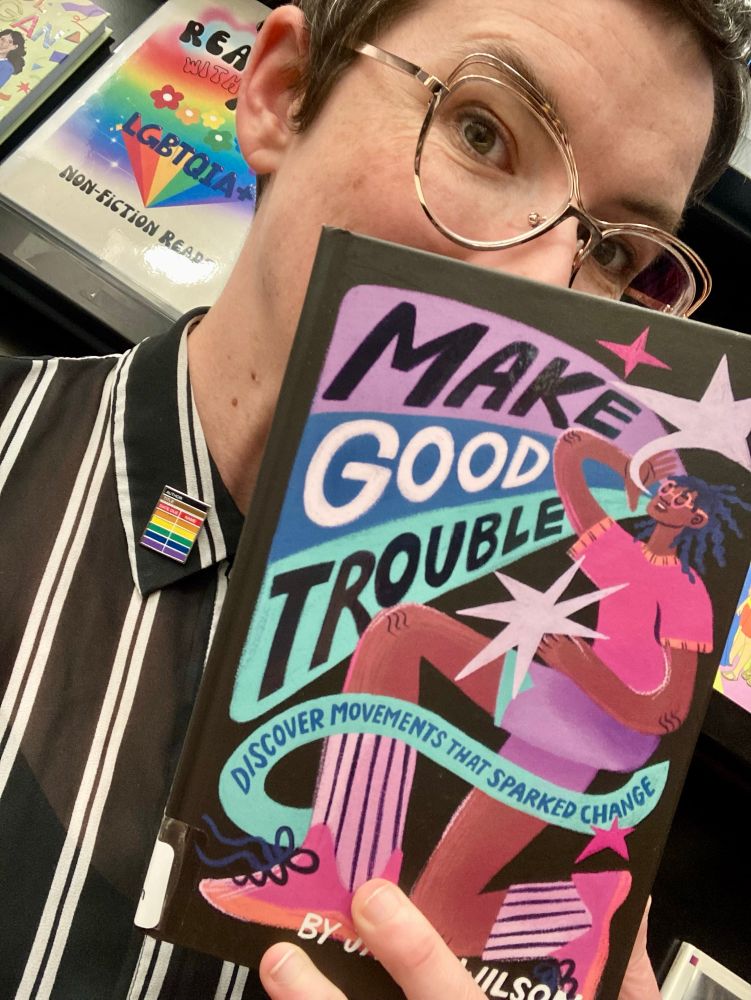 D holding the book Make Good Trouble by Jamia Wilson.