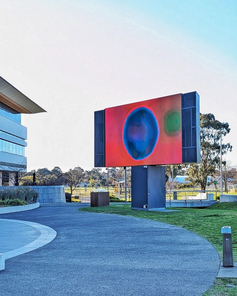 Video artwork "Orbs + Deep Pink" on large outdoor LED screen at Bunjil Place, Naarm/Melbourne, park and playing fields in background. The sky is clear blue and the light is a late winter afternoon hue.