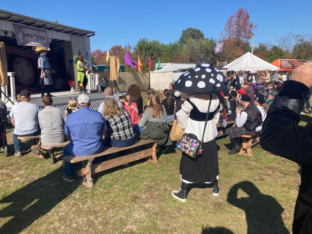 Two comedians on stage in costume worn a crowd looking, many in costume themselves.