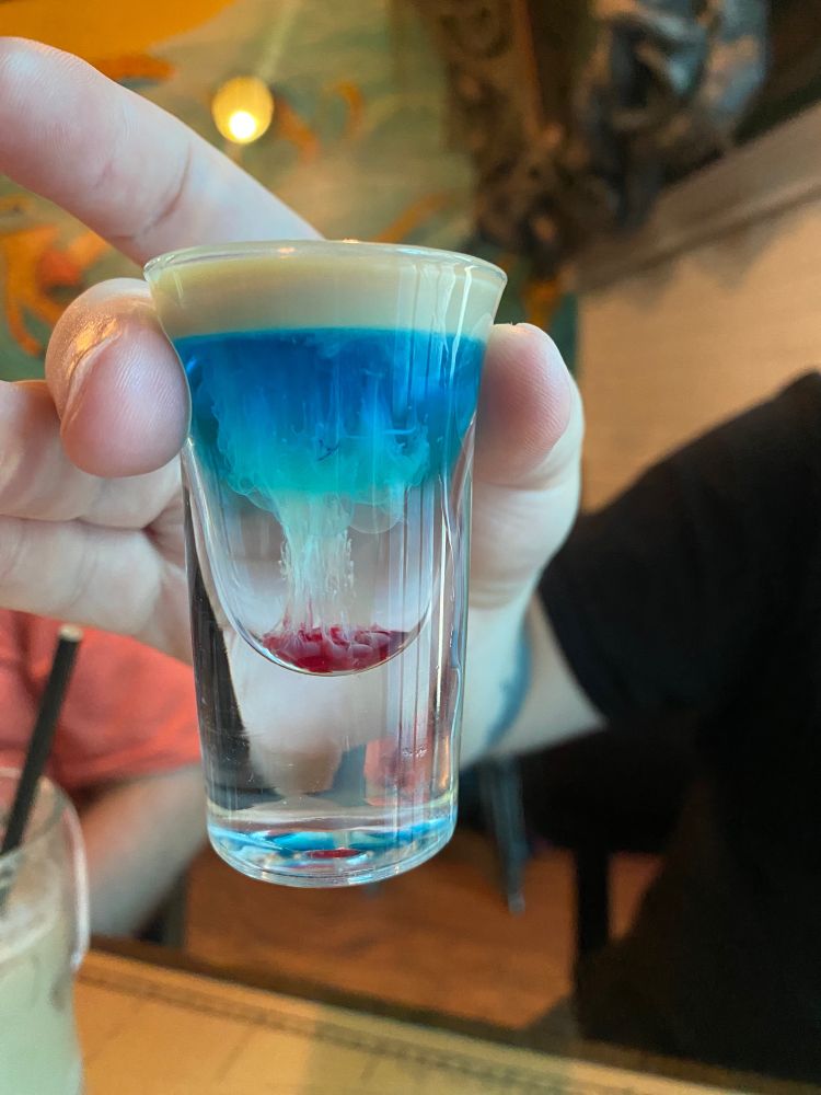 Photo of a hand holding a shot glass with a layered alcoholic drink.