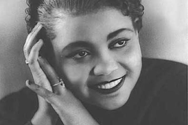 Close of up of Ruby Elzy, a woman with black fingerwave curly hair, dark eyes, dark brown skin, and lipstick framing a coy smile